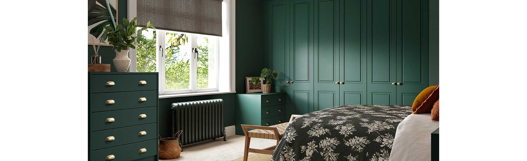 Cozy bedroom with dark green walls and furniture, a floral bedspread, woven rug, and a large window allowing natural light. Calm and inviting atmosphere.