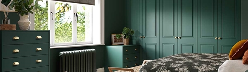 Cozy bedroom with dark green walls and furniture, a floral bedspread, woven rug, and a large window allowing natural light. Calm and inviting atmosphere.