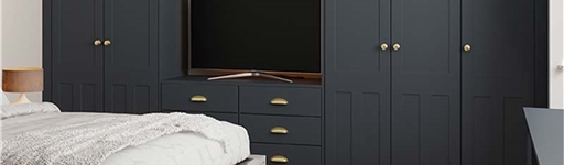 Modern bedroom with dark blue wardrobes, a large TV, and a cozy bed with a textured blanket. A light gray rug and wooden floor add warmth.