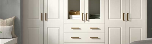 Spacious bedroom with white wardrobes, wooden handles, and glass panels. Light wood floor, fluffy rug, and a cozy vibe with a small side table and soft lighting.