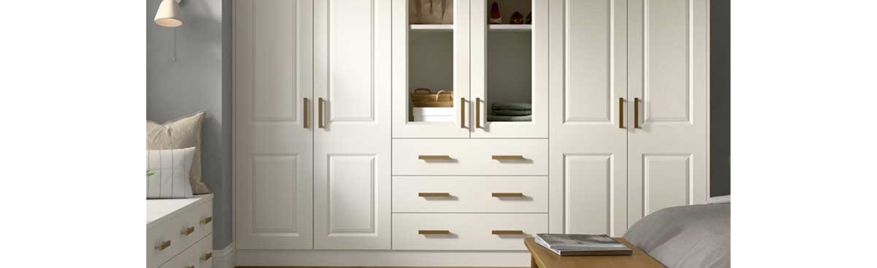 Spacious bedroom with white wardrobes, wooden handles, and glass panels. Light wood floor, fluffy rug, and a cozy vibe with a small side table and soft lighting.
