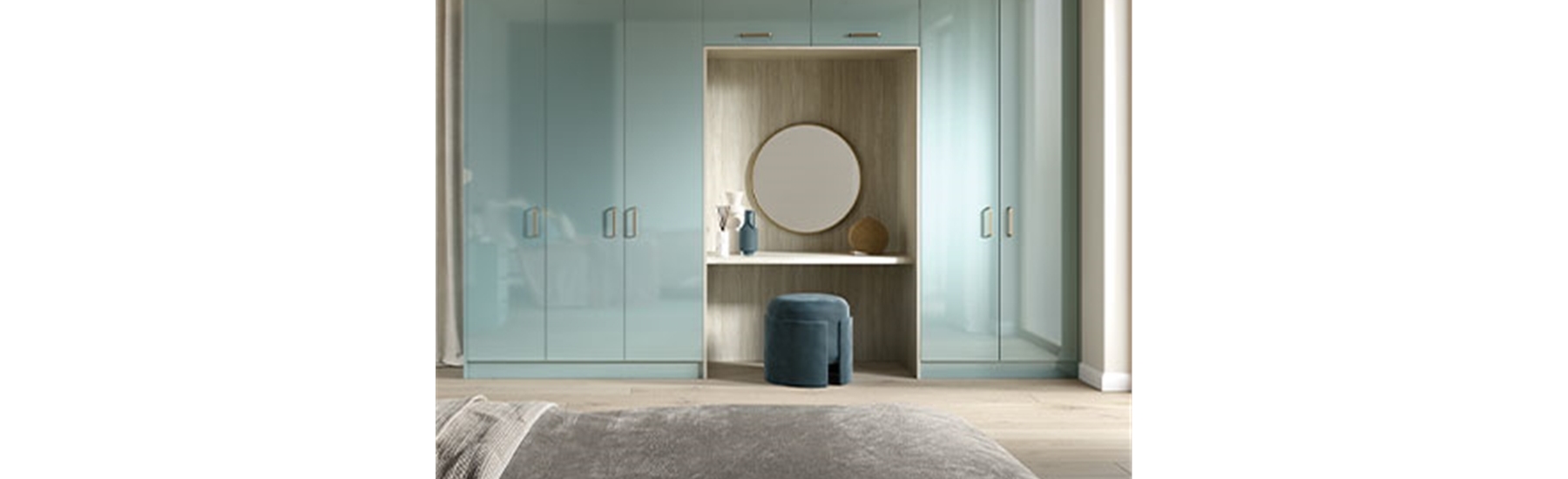 A modern bedroom features glossy pastel blue wardrobes with integrated vanity. A round mirror, decorative vases, and a soft velvet stool complete the elegant look.